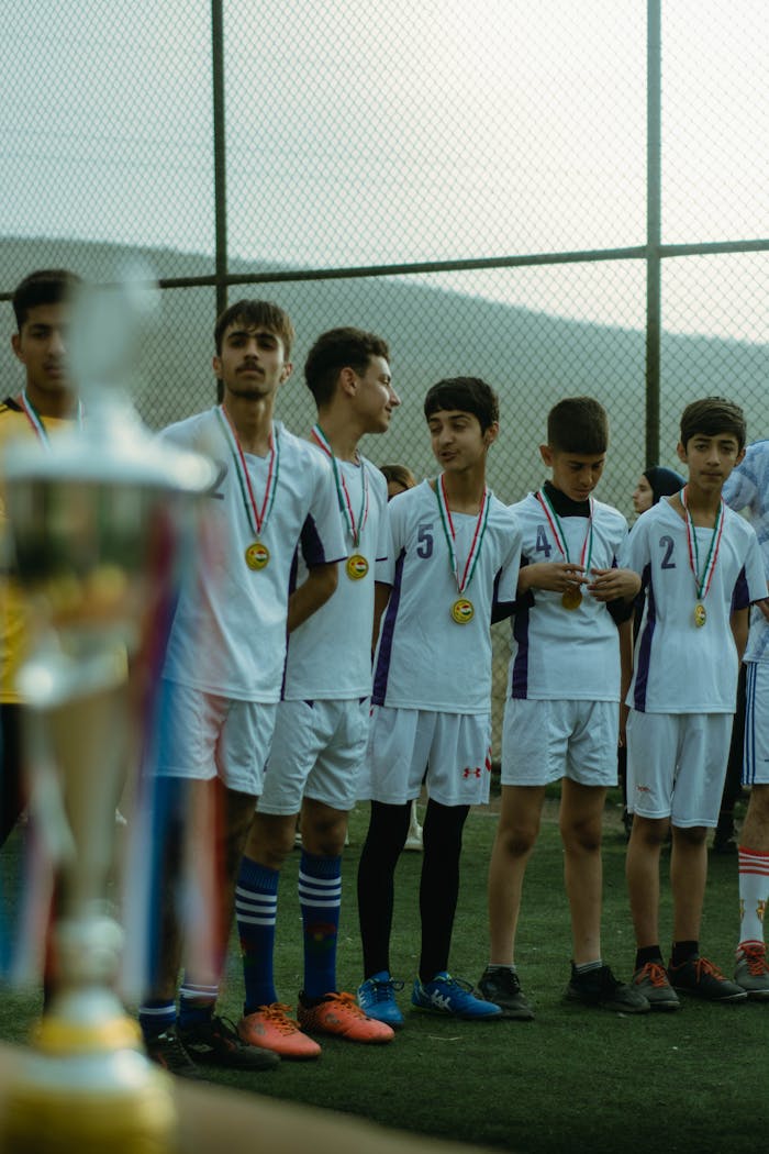gallery-2 Teenage soccer team in Erbil celebrating victory with medals on outdoor field.