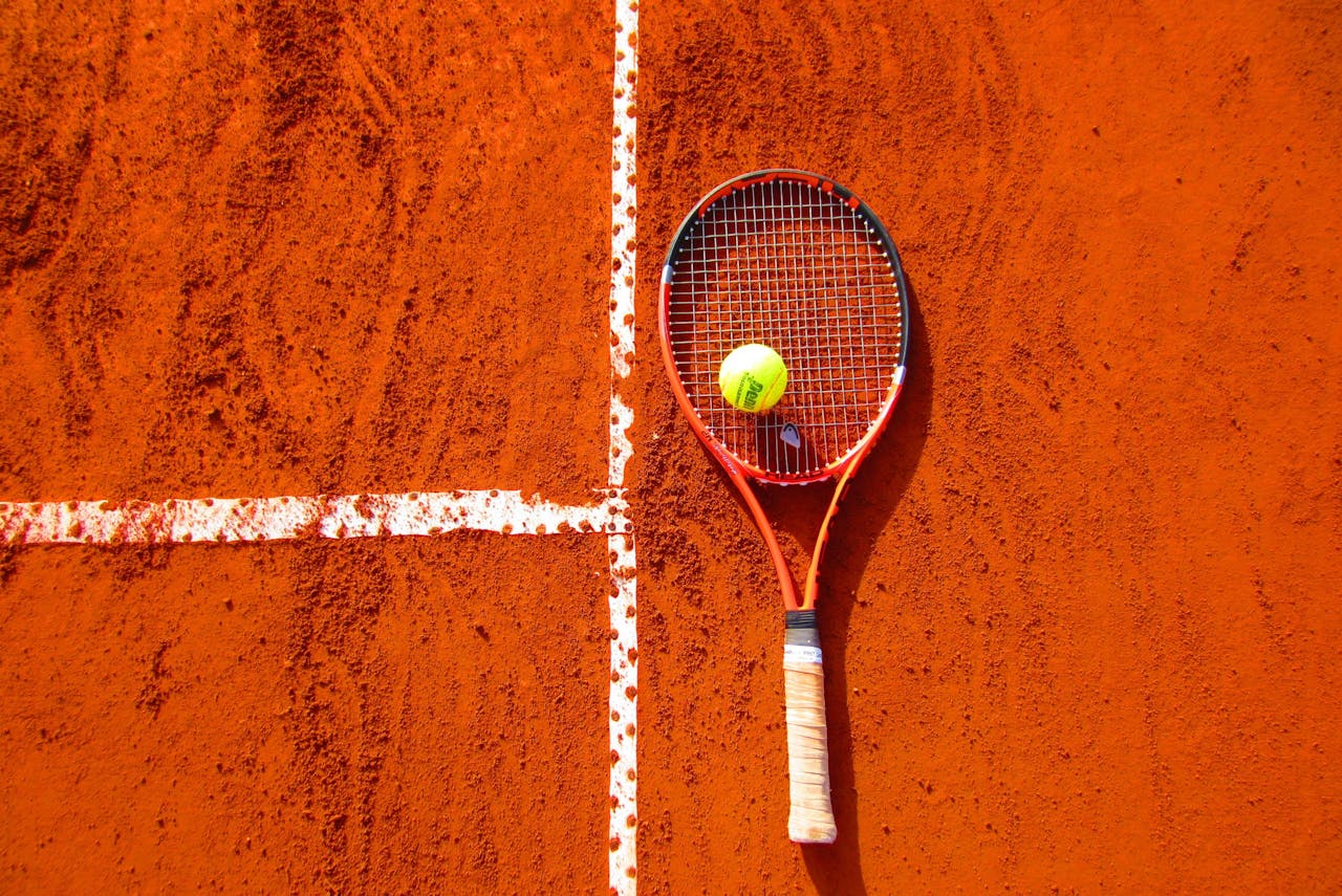 hero-img-01 Tennis racket and ball on red clay court, ideal for sports-themed content.