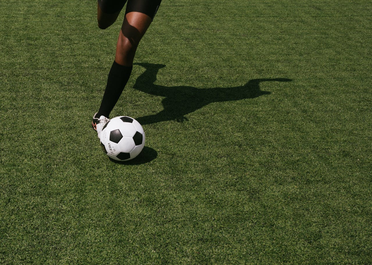 our-services-2 Cropped shot of a soccer player in motion, performing a kick on a grassy sports field under daylight.