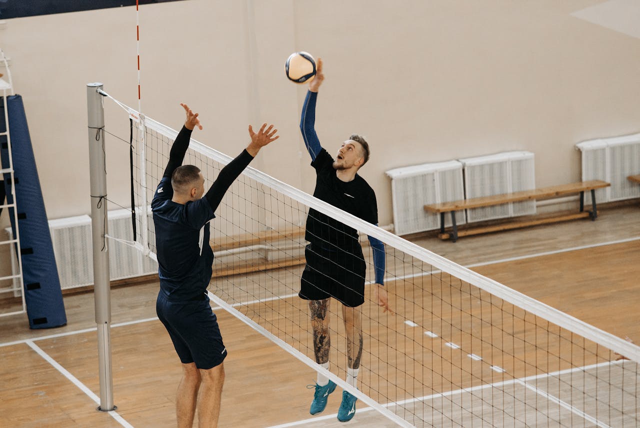 gallery-5 Two male athletes playing a competitive volleyball game indoors.