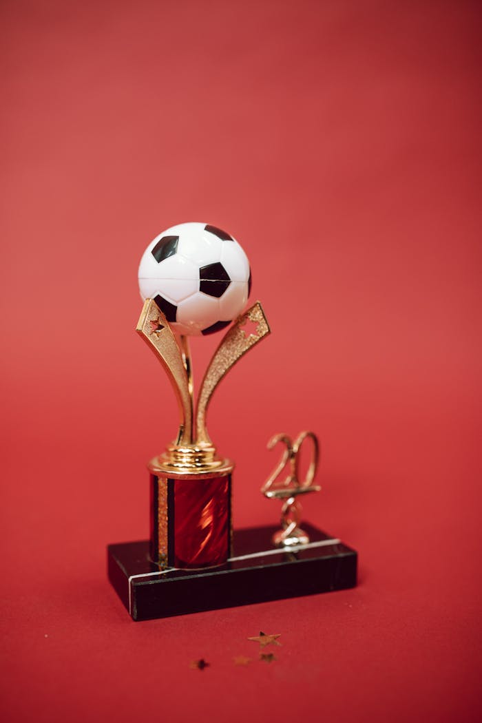 contact-img Elegant golden soccer trophy with red accents and soccer ball top on a red background.
