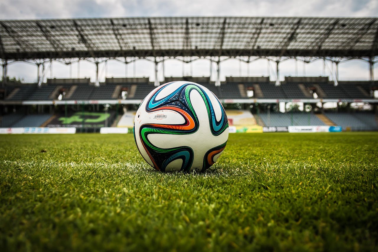 about-01 A vibrant soccer ball rests on a lush green field inside an empty stadium, capturing the essence of sports.